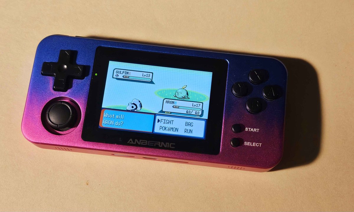 A handheld game console with a purple-pink gradient metal case. On the screen is a screen from the game Pokemon Emerald.